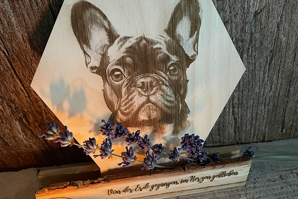 Eckiges Holzschild, verziert mit der Gravur eines Hundes. Darunter ein emotionaler Spruch und ein paar Blumen