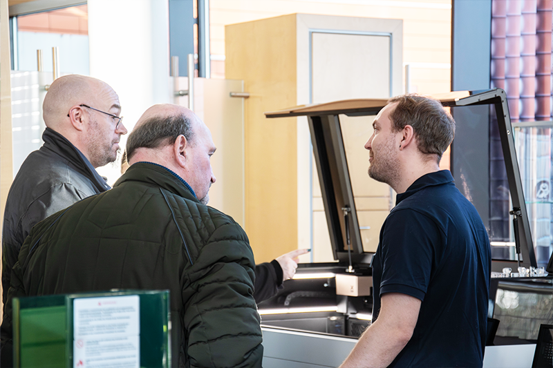 Ein Laserlinkmitarbeiter berät zwei Kunden vor einem xTool P2S Lasergerät