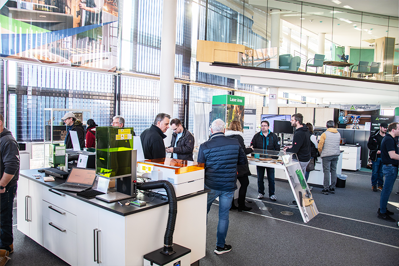 viele Menschen stehen in einem Raum mit verschiedenen xTool Lasergeräten und lassen sich beraten