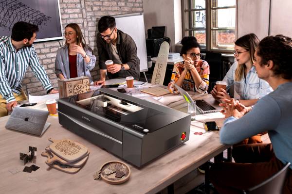 Eine Gruppe von Menschen Sitzen um einen xTool Laser, der auf einem Tisch steht, und erstellen verschiedene Modelle aus Holz.